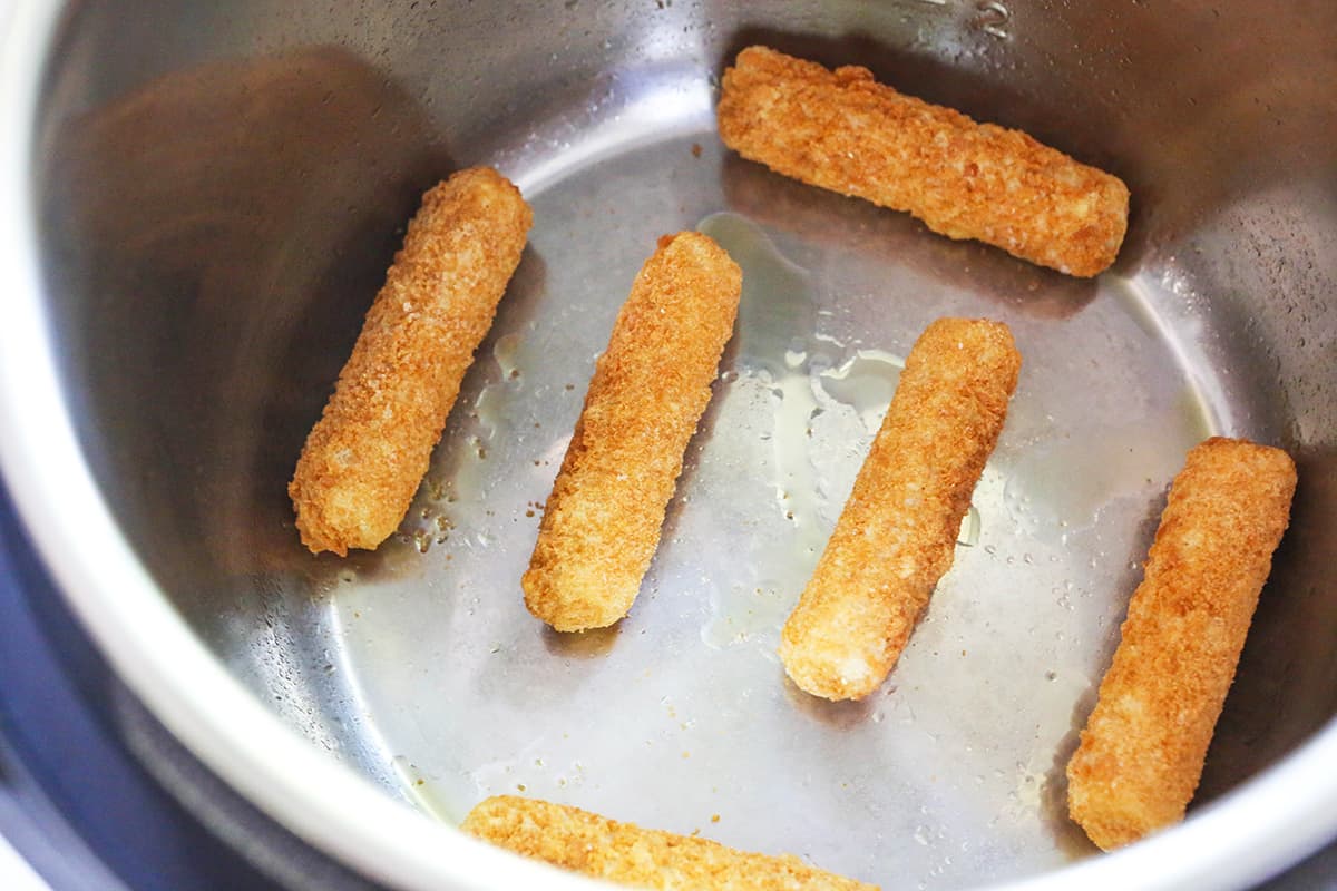Frozen mozzarella sticks in a single layer in an air fryer.