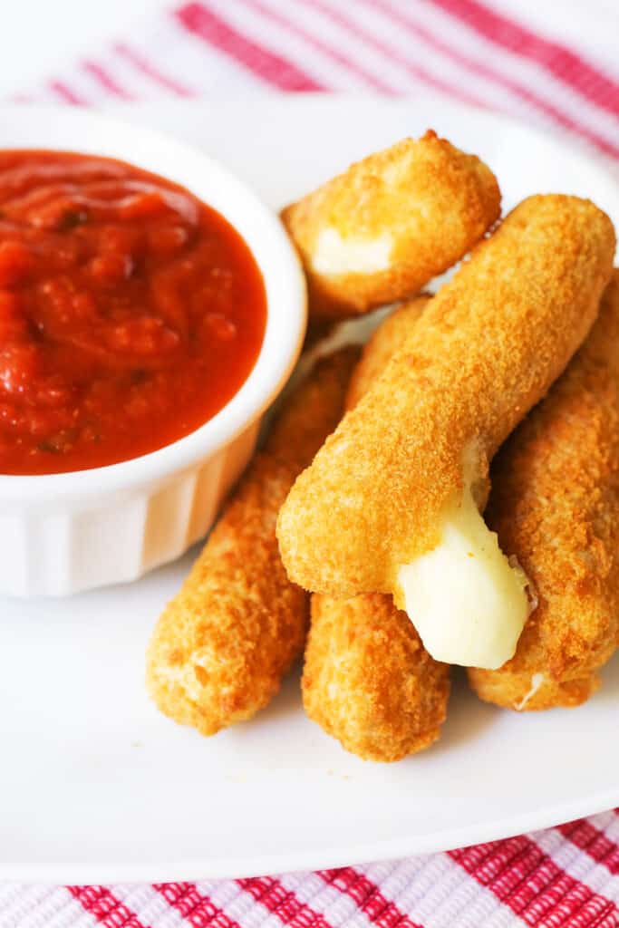 Marinara in a cup next to mozzarella sticks on a plate. 