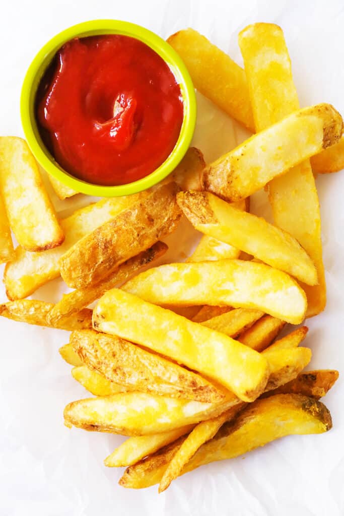 Air fryer frozen steak fries on parchment paper with some ketchup. 