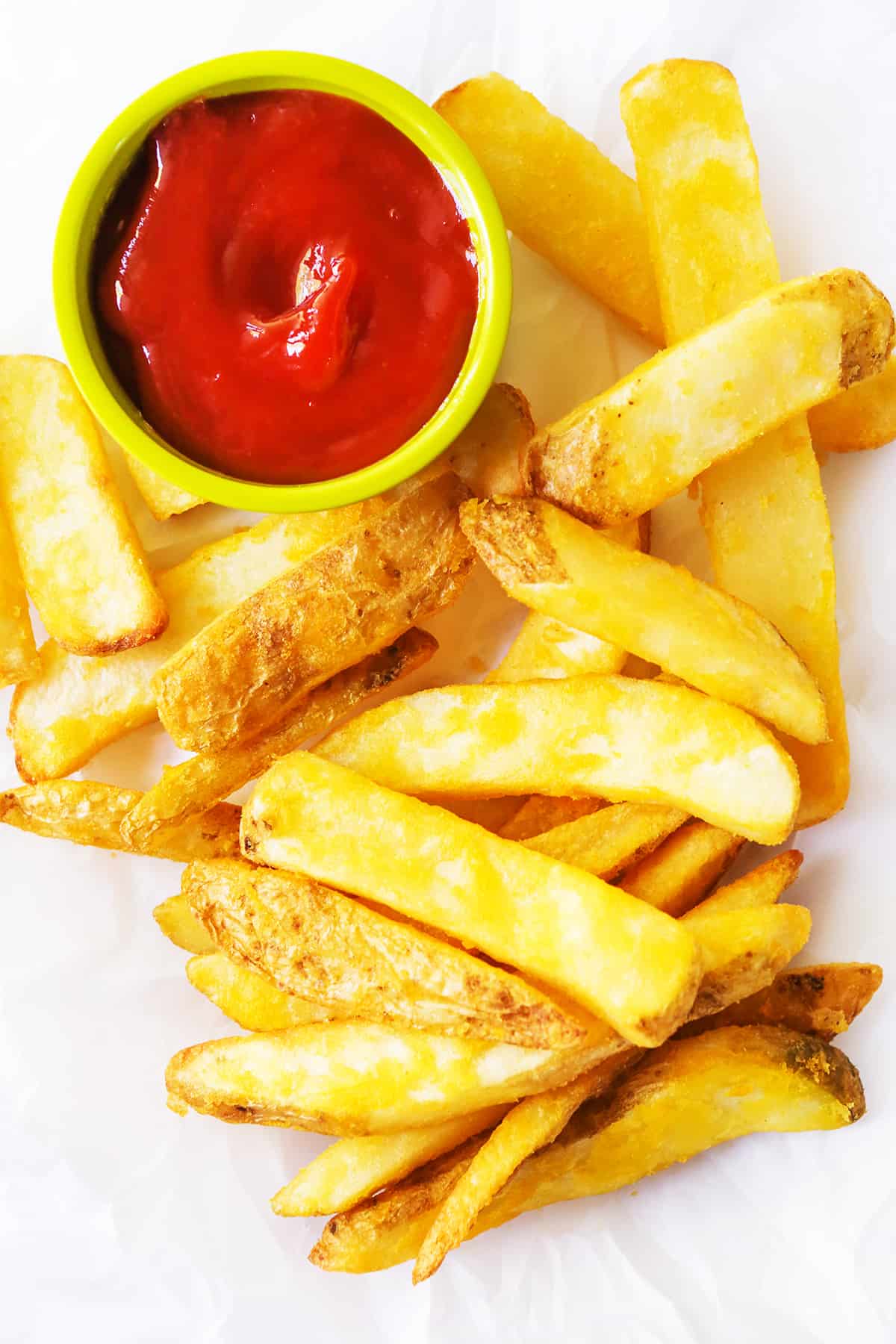 Top view of steak fries stacked on parchment next to ketchup.