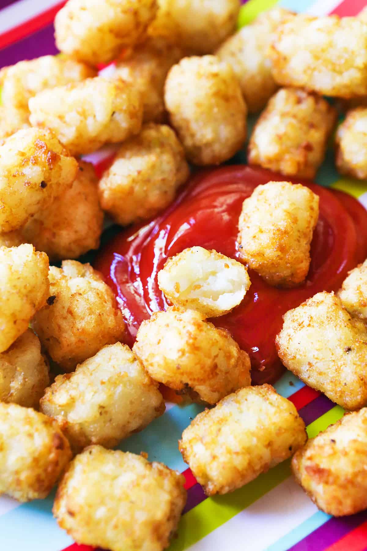 Ketchup surrounded by tater tots, with a bite taken out of one in the middle.