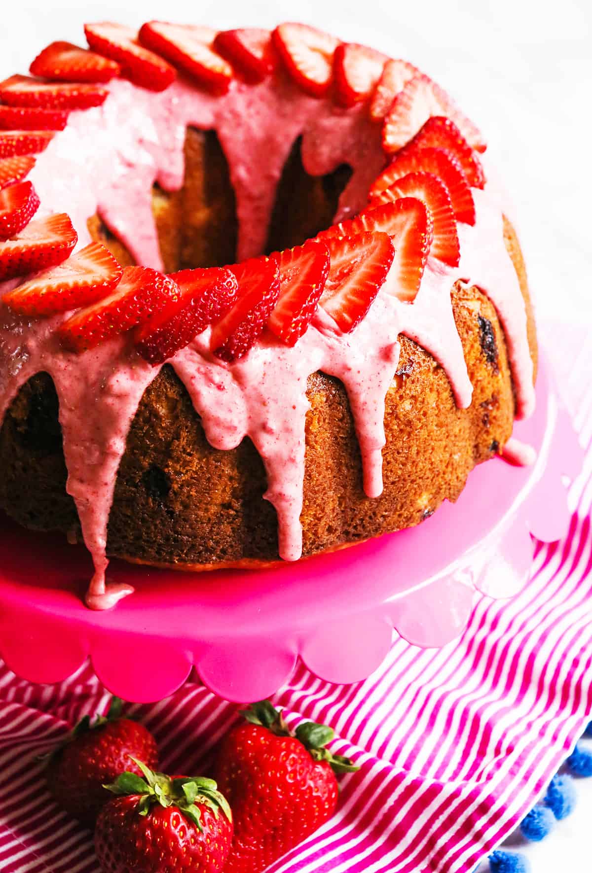 Looking down onto a strawberry bundt cake drizzled with glaze and topped with fresh strawberry slices.