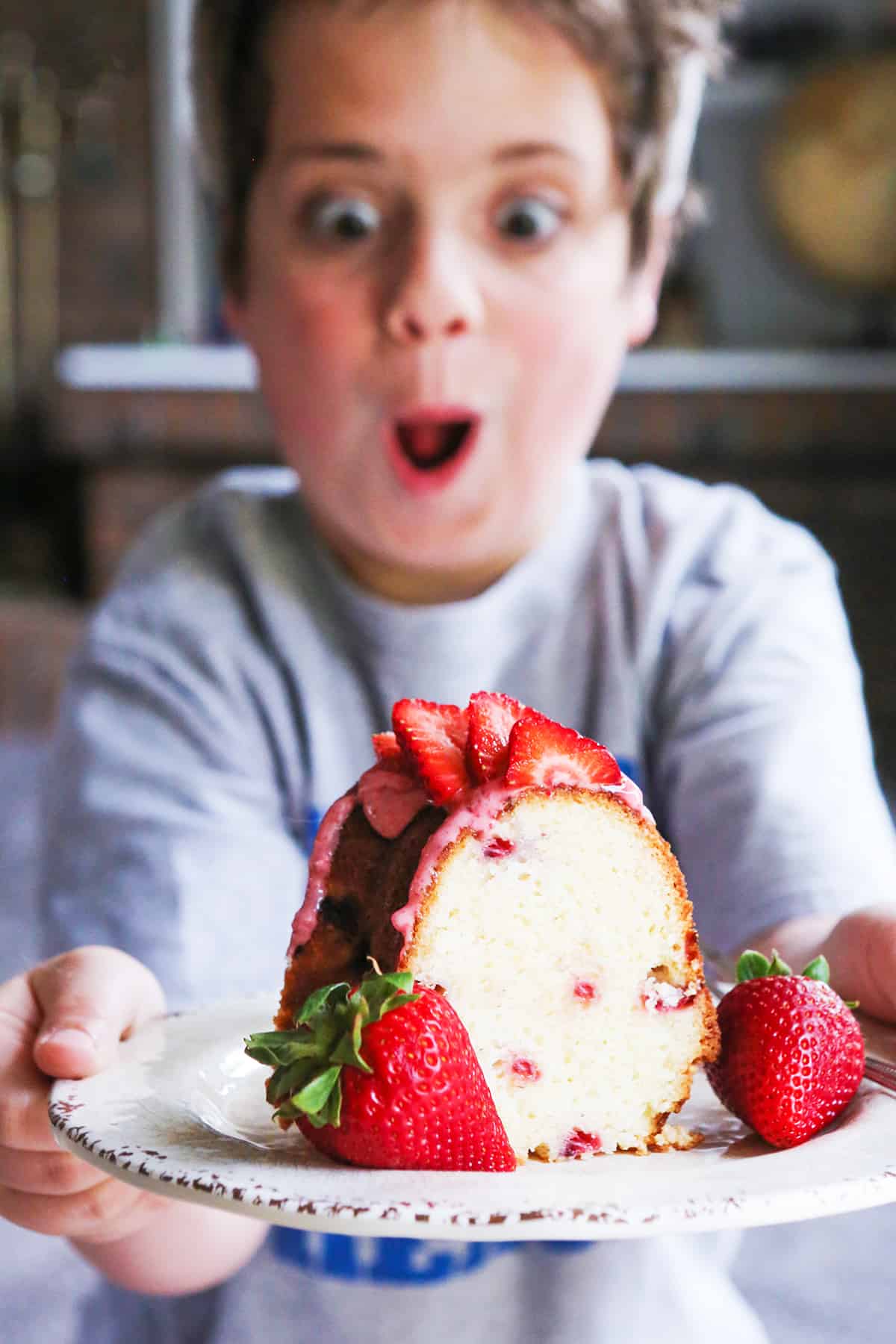 A cute boy with a surprised and happy face, staring at a piece of strawberry cake.