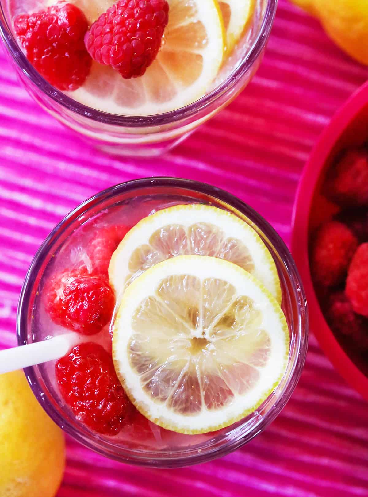 top view of 2 glasses of raspberry lemonade with lemon slices and raspberries on top