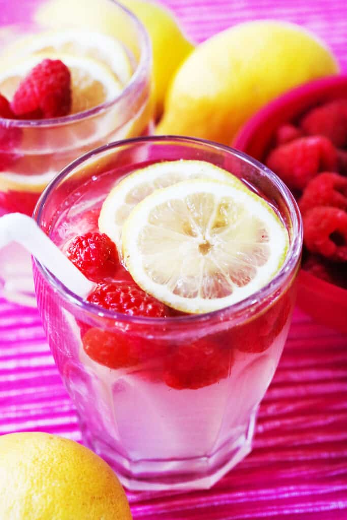 Glass of raspberry lemonade garnished with a straw, raspberries and lemon slices