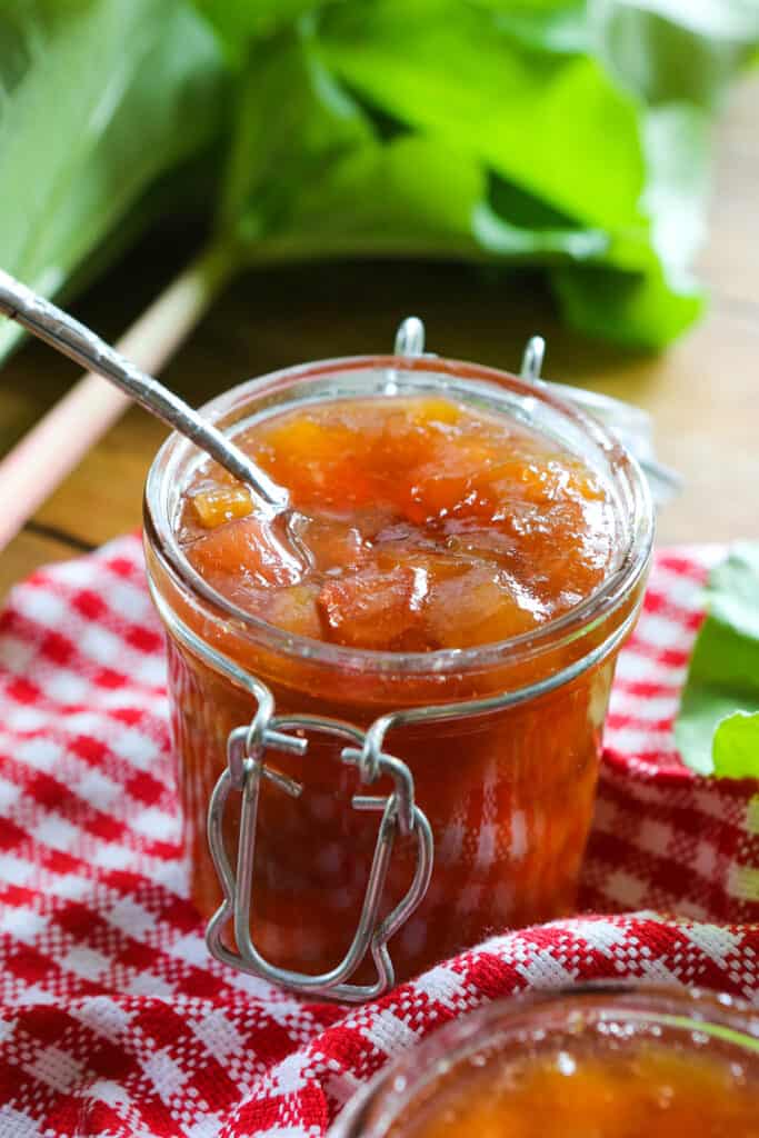 Spoon sticking out of rhubarb peach jam in a glass jar. 