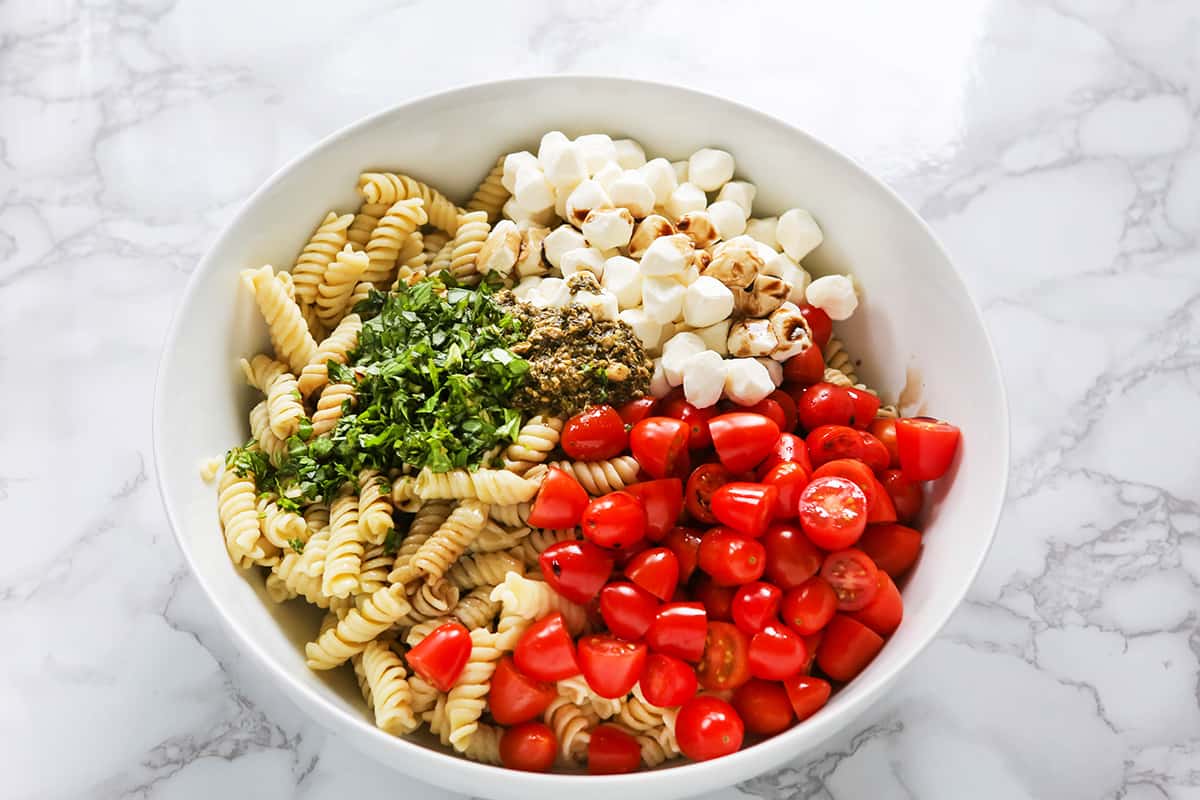 Bowl filled with caprese pasta salad recipe ingredients.
