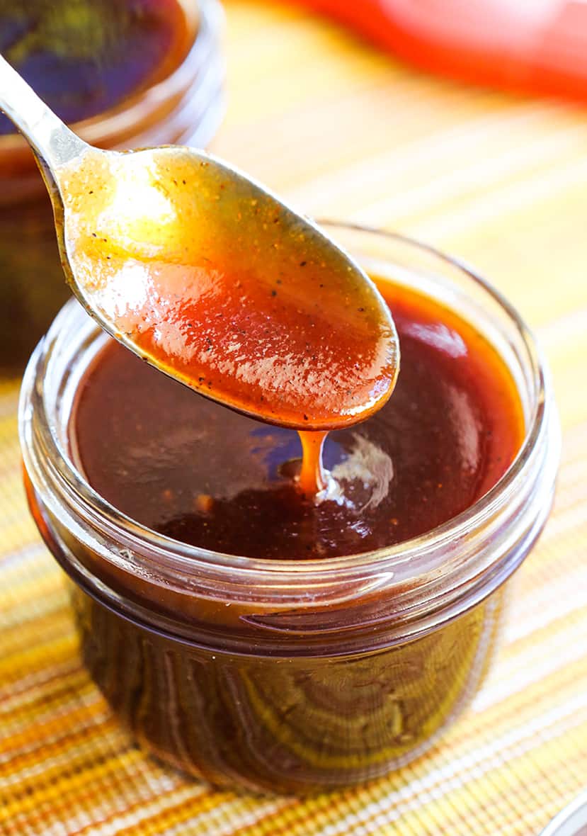 Spoon dripping bbq sauce into a small mason jar.