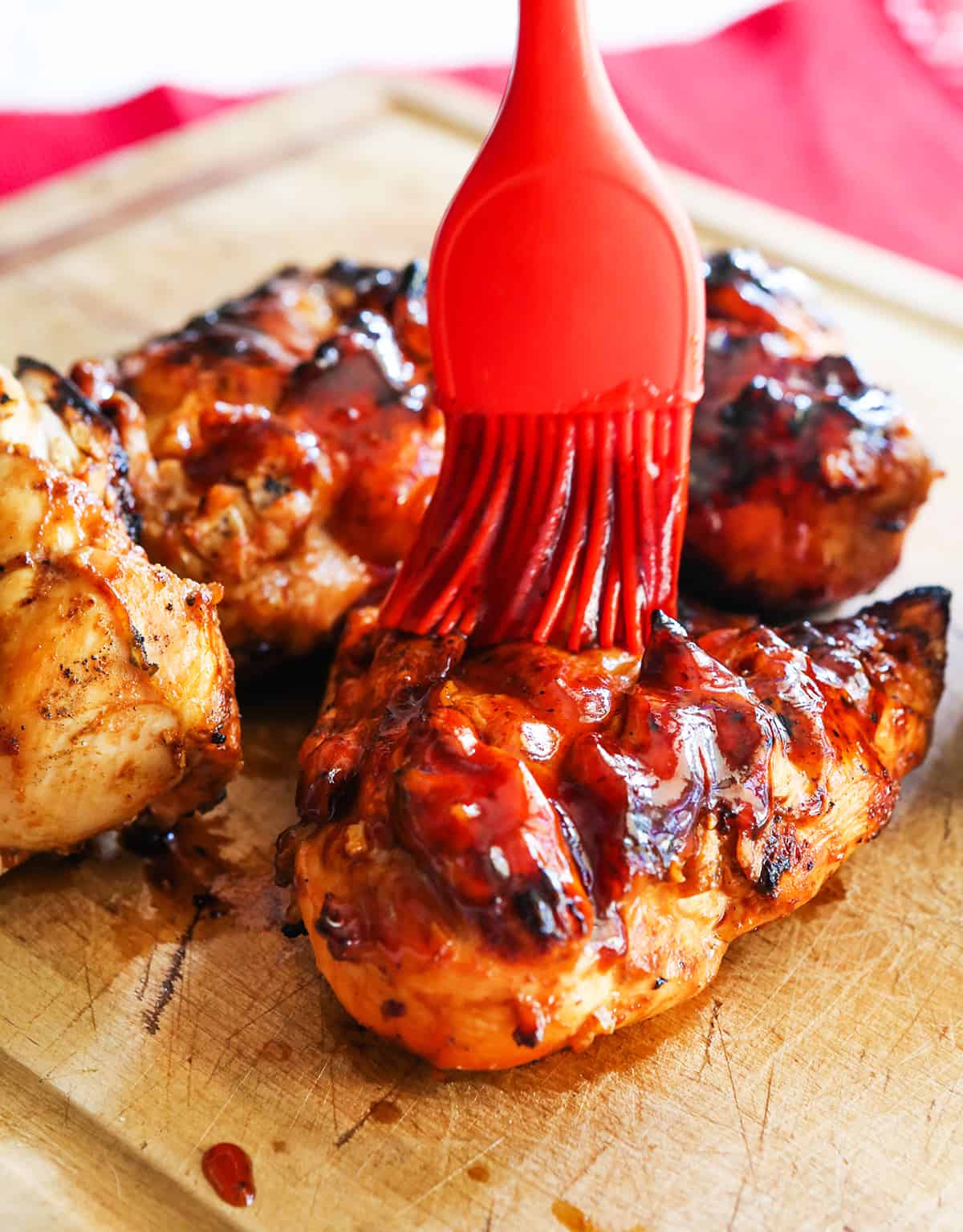 basting brush spreading bbq sauce over grilled chicken