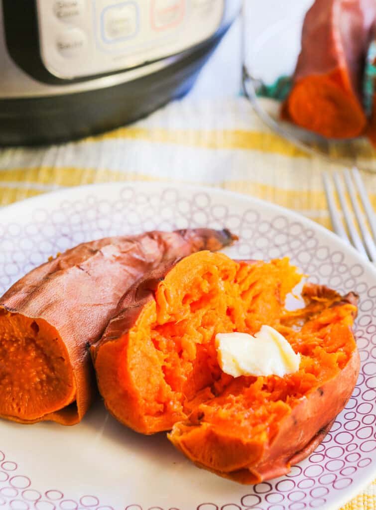 A sweet potato cooked in the Instant Pot behind the plate is cut in half and mashed with a pat of butter melted on top. 