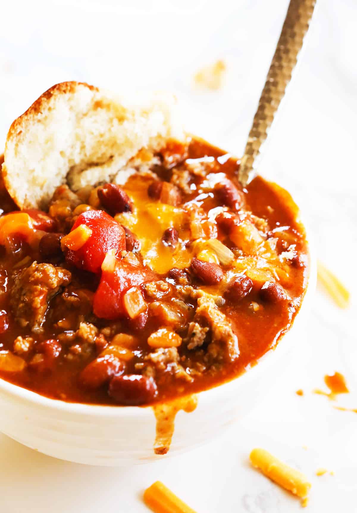 Bowl of chili with melted cheese on top and a piece of bread stuck in the side.