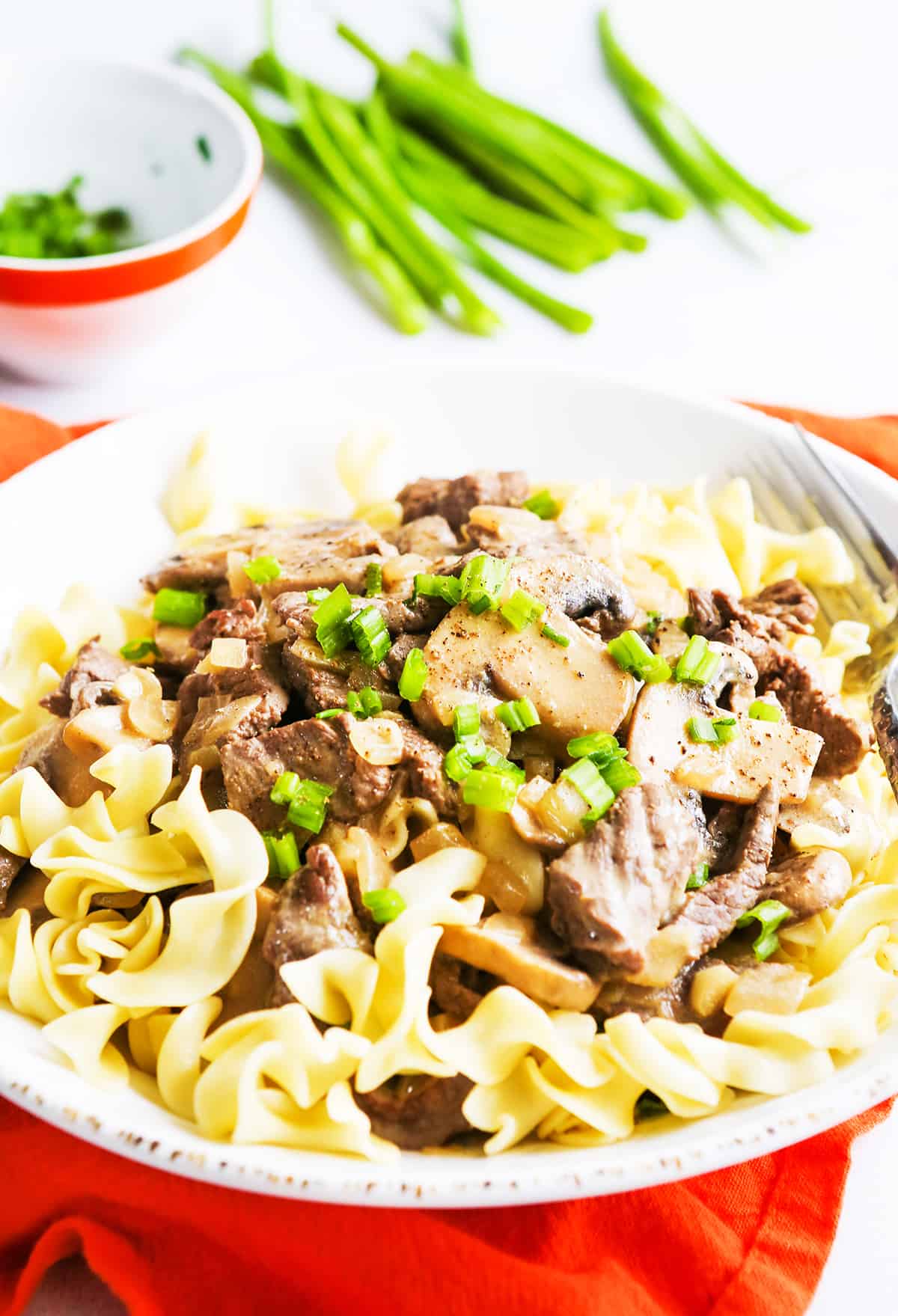 cooked egg noodles topped with beef and mushrooms sitting next to green onions