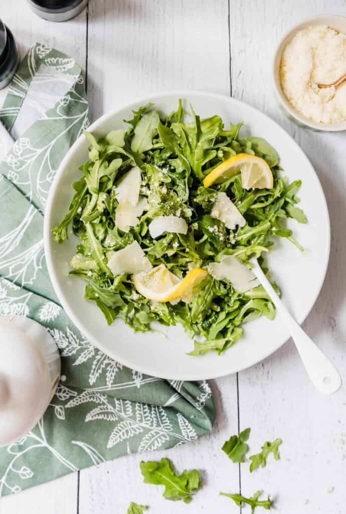 italian arugula salad with shaved parmesan and half slices of lemon in a bowl with a fork sticking out