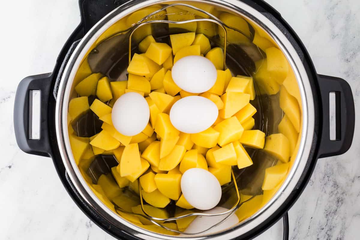 Instant Pot with trivet inside and chopped potatoes on top, along with four eggs.
