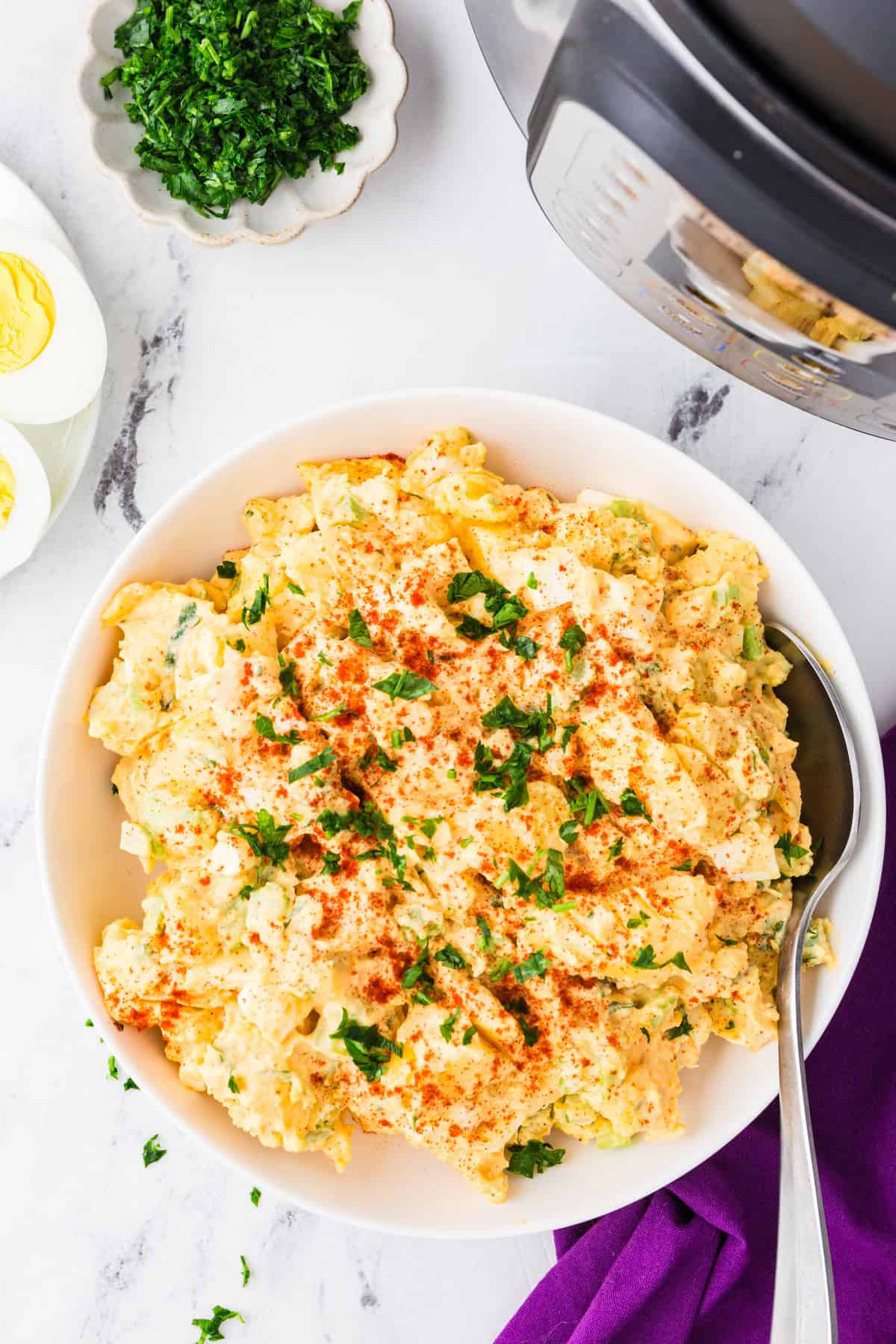 Serving bowl with potato salad inside and a serving spoon stuck inside, next to an Instant Pot.