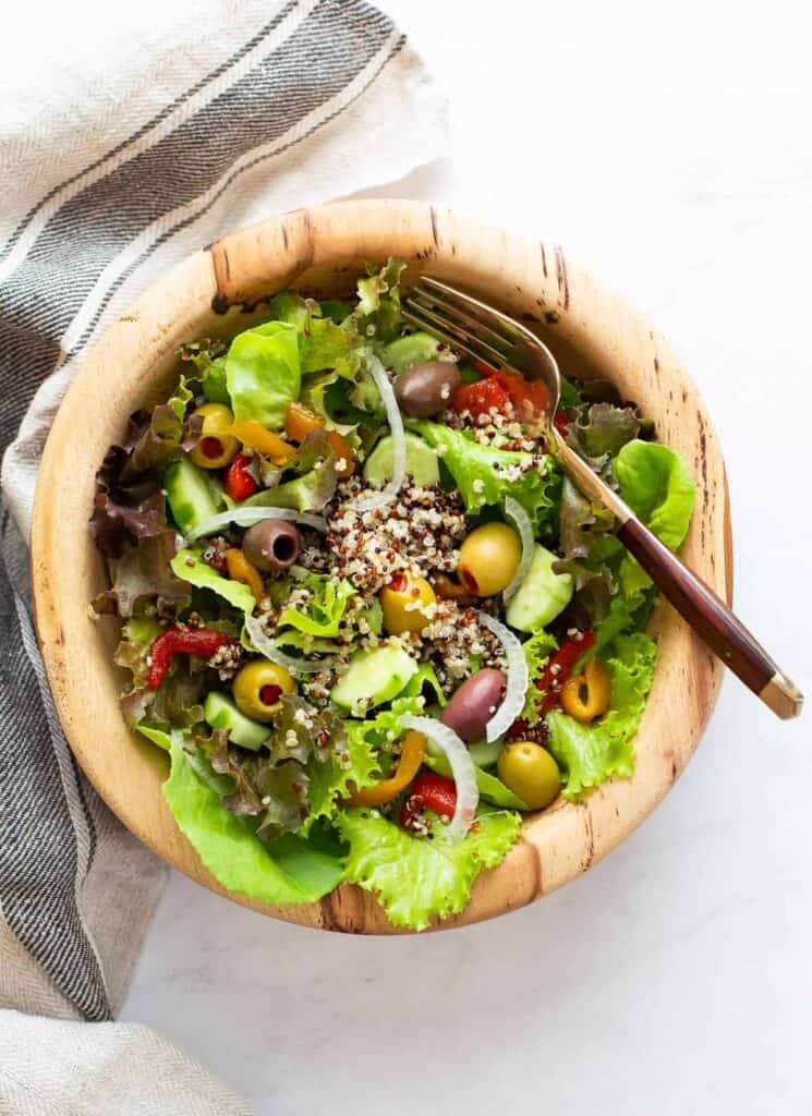 top view of leafy green salad topped with quinoa and olives