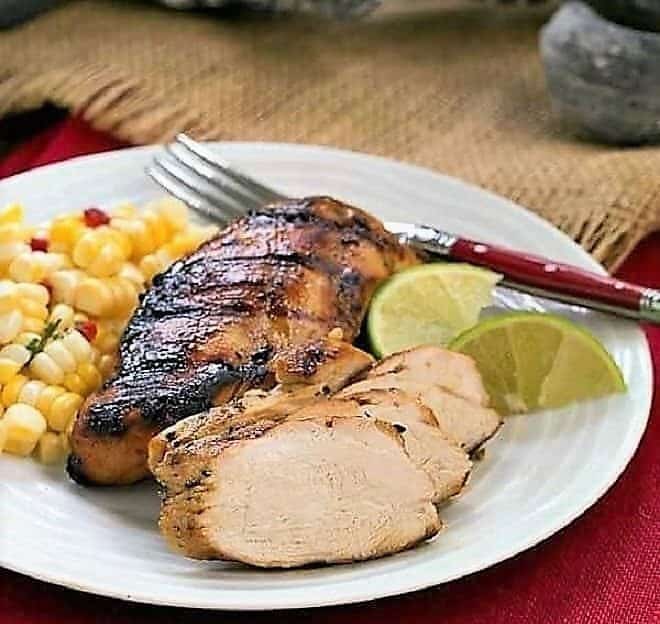 sliced pieces of mustard, garlic, lime marinated chicken breasts on a plate with a side of corn 