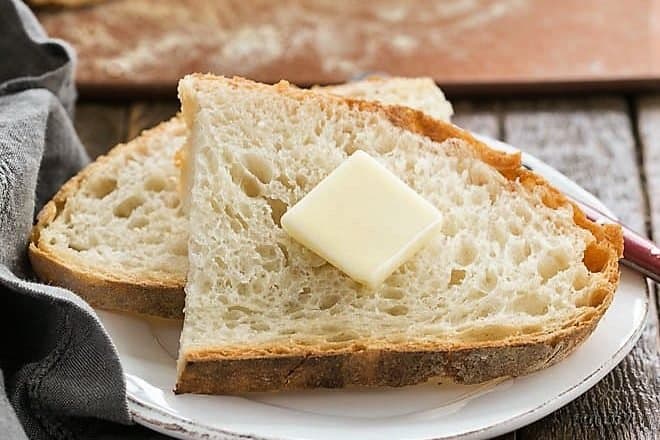 two slices of no knead bread on a small plate and a pat of butter on top 