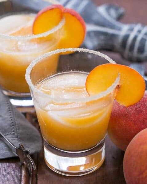 fresh peach margaritas with a sugar rim around the glass and a peach slice garnish