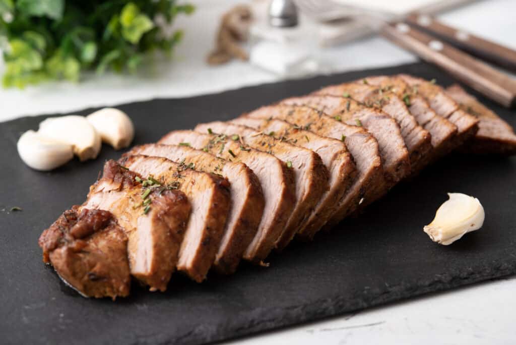 sliced instant pot roast beef on a cutting board and whole garlic garnish alongside