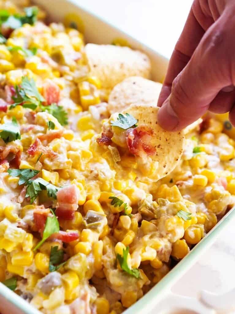 Hand scooping up corn dip onto a tortilla chip. 