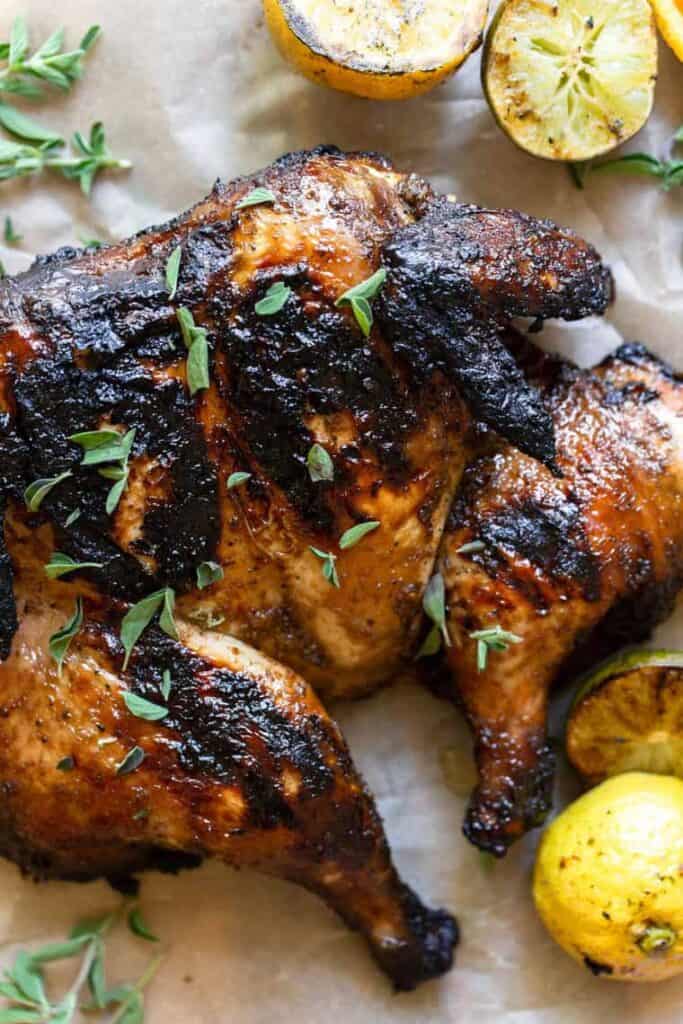 grilled spatchcock chicken on parchment paper alongside a whole lemon