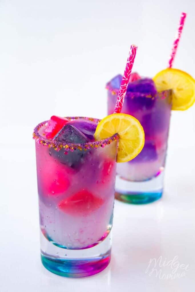 unicorn lemonade in 2 tall glasses with a colorful sugar rim and garnish of a lemon slice with straws