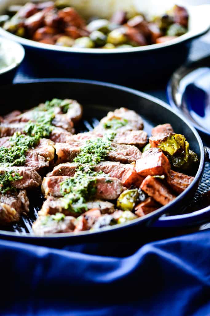 strip loin with veggies cooking in a cast iron pan with chimichurri sauce drizzled on top