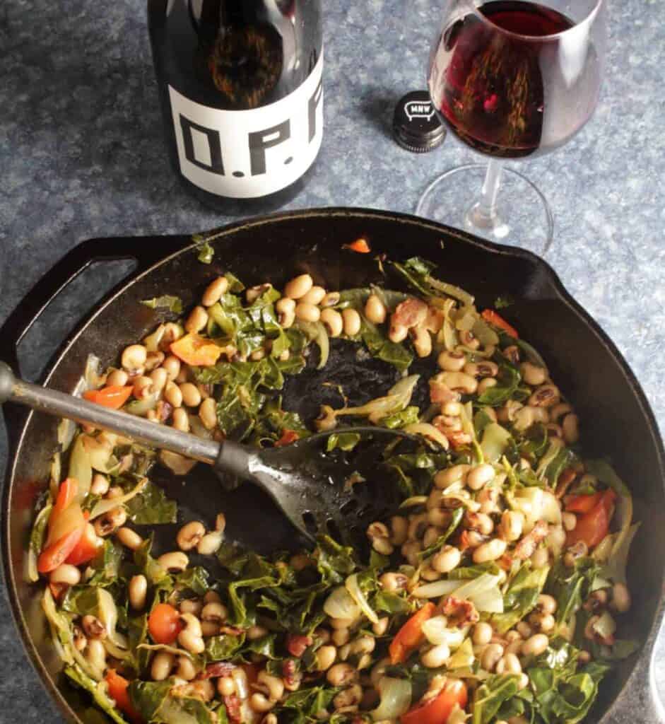 cast iron pan with a spatula in a bed of black-eyed peas with collard greens