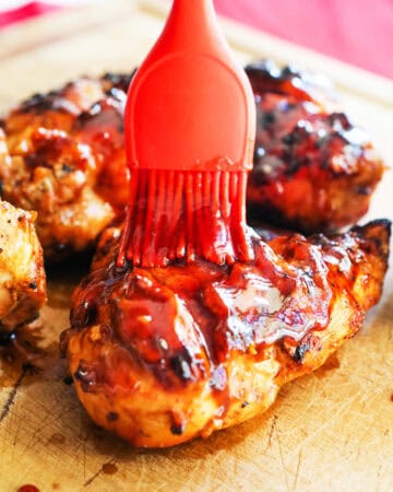 Baked BBQ chicken being glazed with ketchup using a silicone brush.