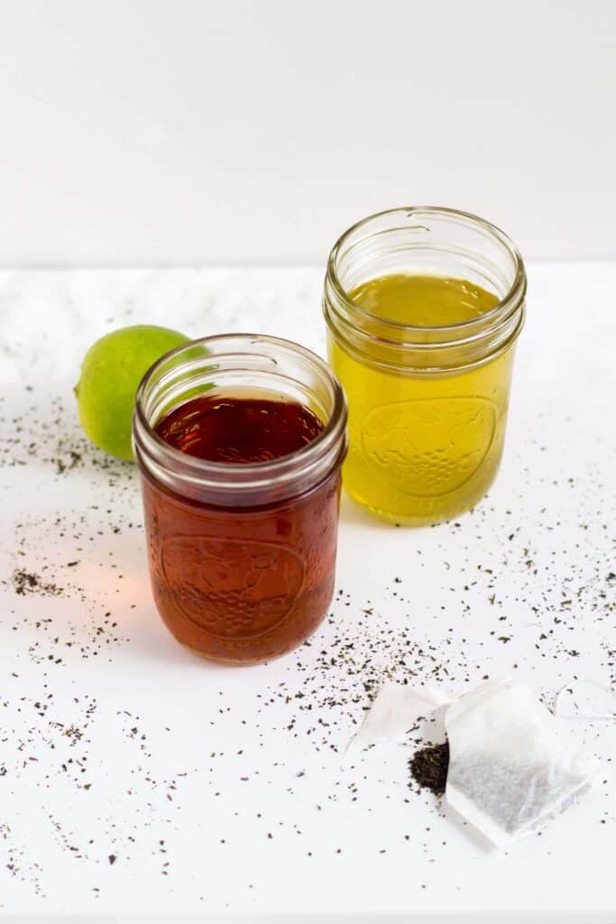 two mason jars with cold brew tea next to a lime and open tea bag on the table