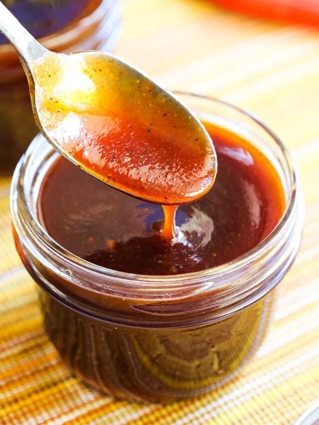 Spoon drizzling bbq sauce into a small mason jar.
