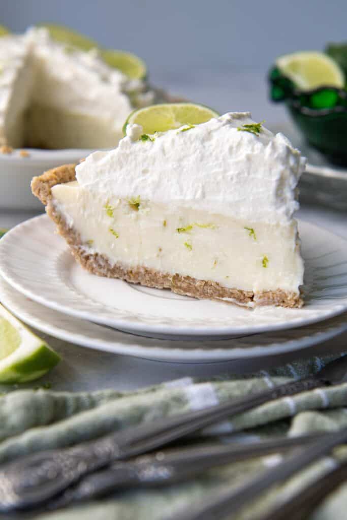 slice of key lime pie on a plate next to the pie plate with lime garnishes on top