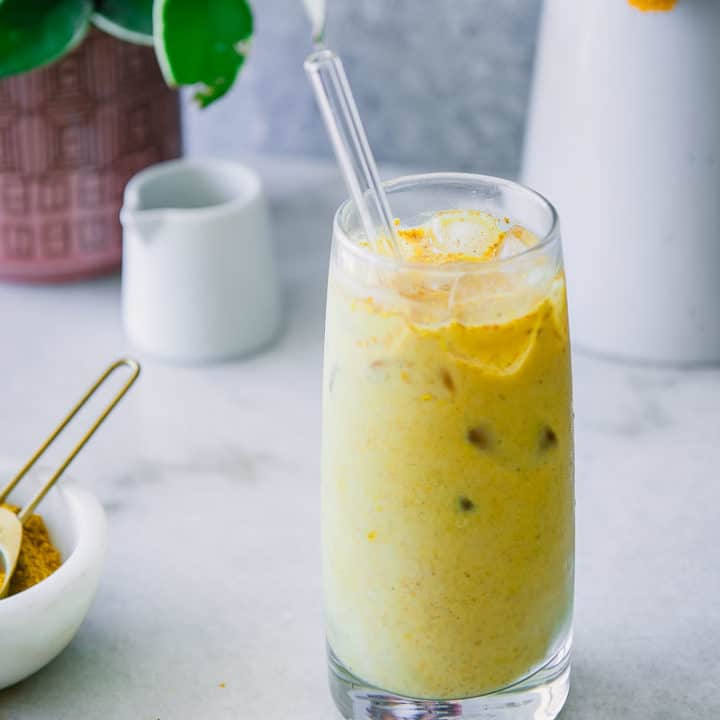 glass of iced golden milk latte with a straw in the glass