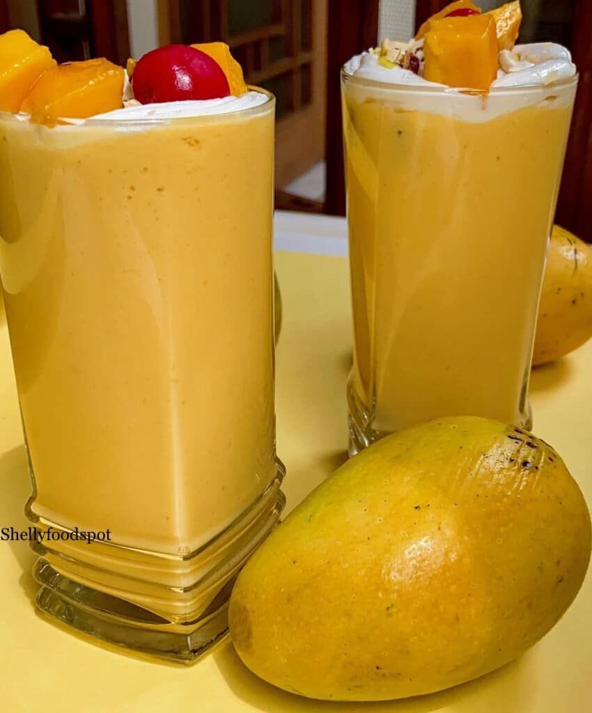 two glasses of mango milkshake wiht a mango garnish and a whole mango sitting in front