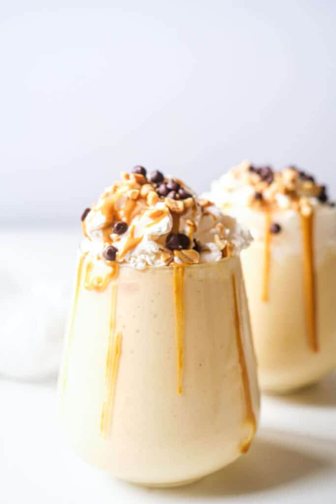 two glasses filled with creamy cookie peanut butter milkshake topped with whipped cream and drizzled with chocolate and toppings