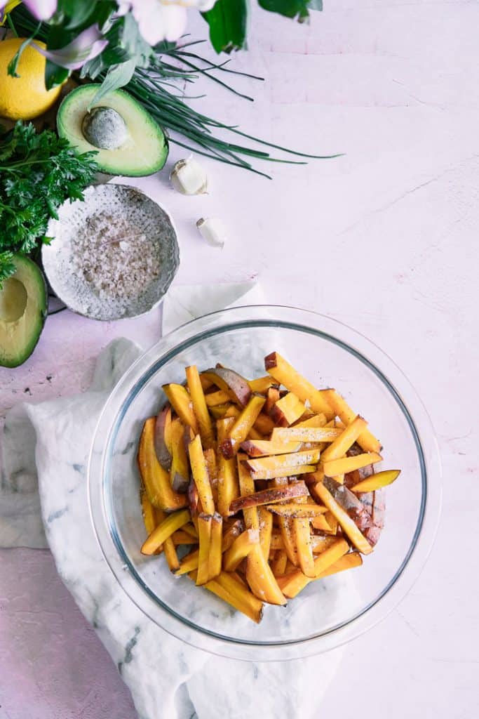 glass bowl of roasted beet fries next to cut open avocados