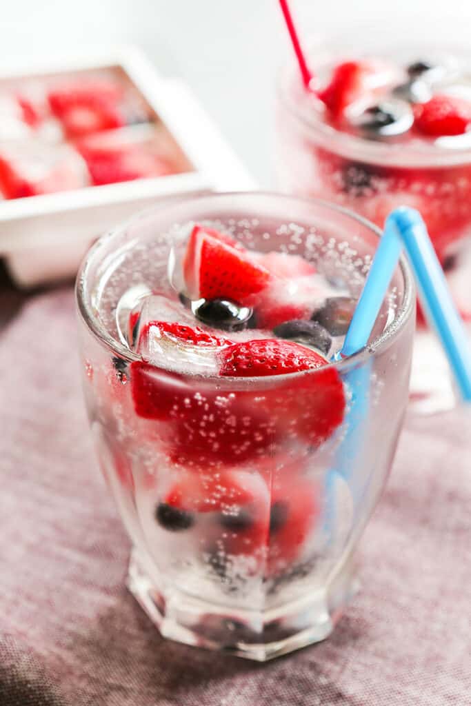 Berries frozen in ice cubes inside a glass of Sprite.