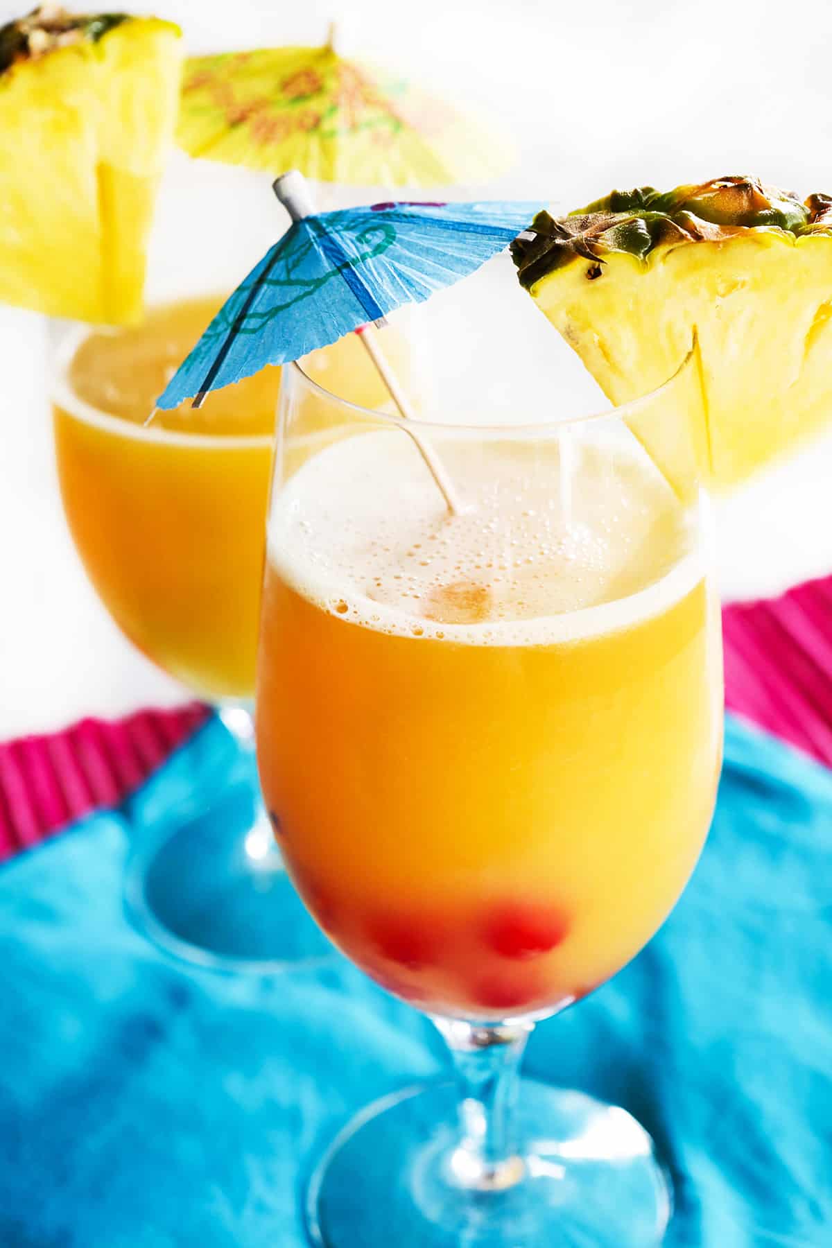 Two glasses of Mai Tais with drink umbrellas and pineapple wedges stuck inside.