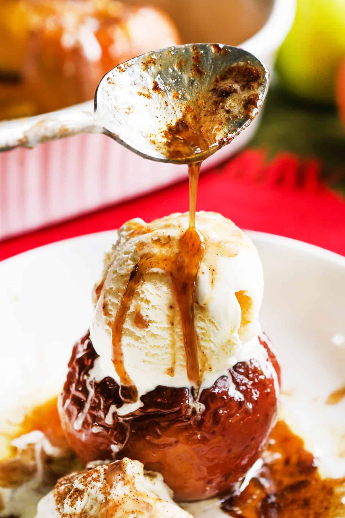 Spoon drizzling caramel over the top of icecream over a baked apple.