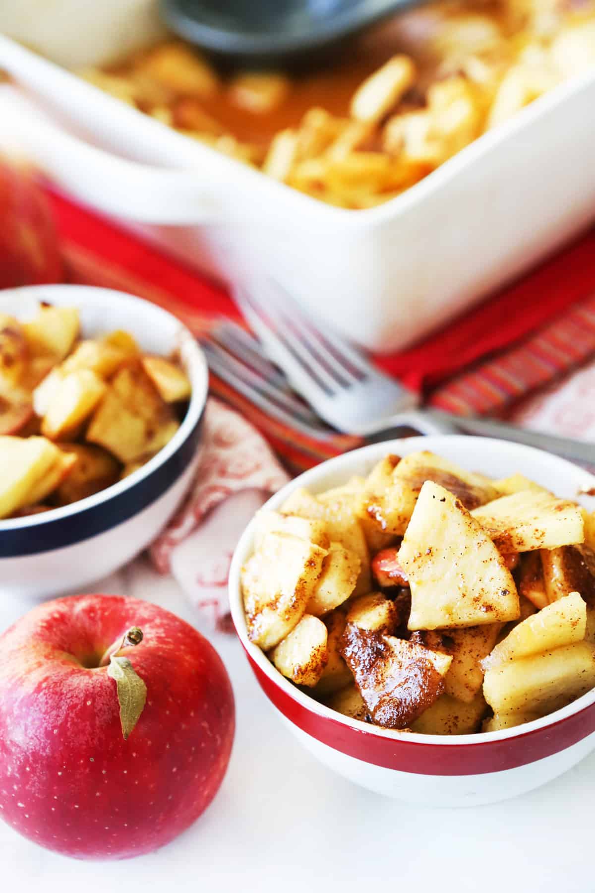Cinnamon baked apples in serving dishes next to baking pan.