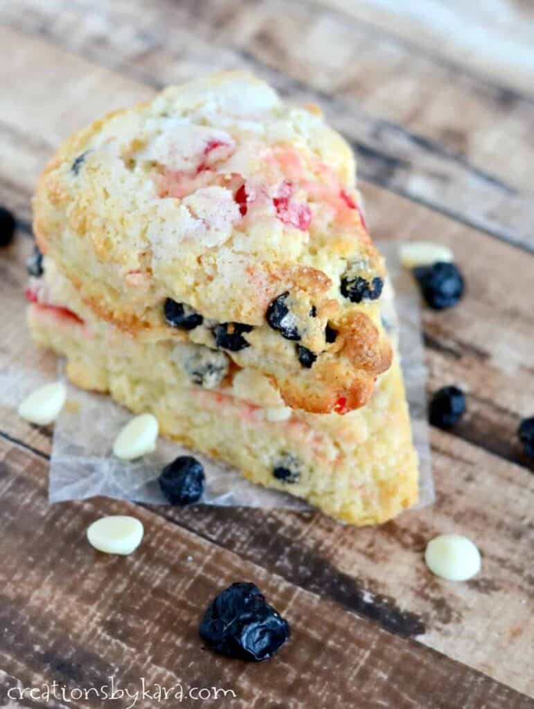 Cherry blueberry scones on a wax piece of paper with dried fruit and white chocolate chips around it.
