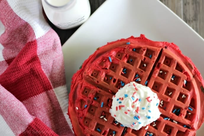 Red waffles with red white and blue sprinkles over the dollop of whipped cream on a plate. 