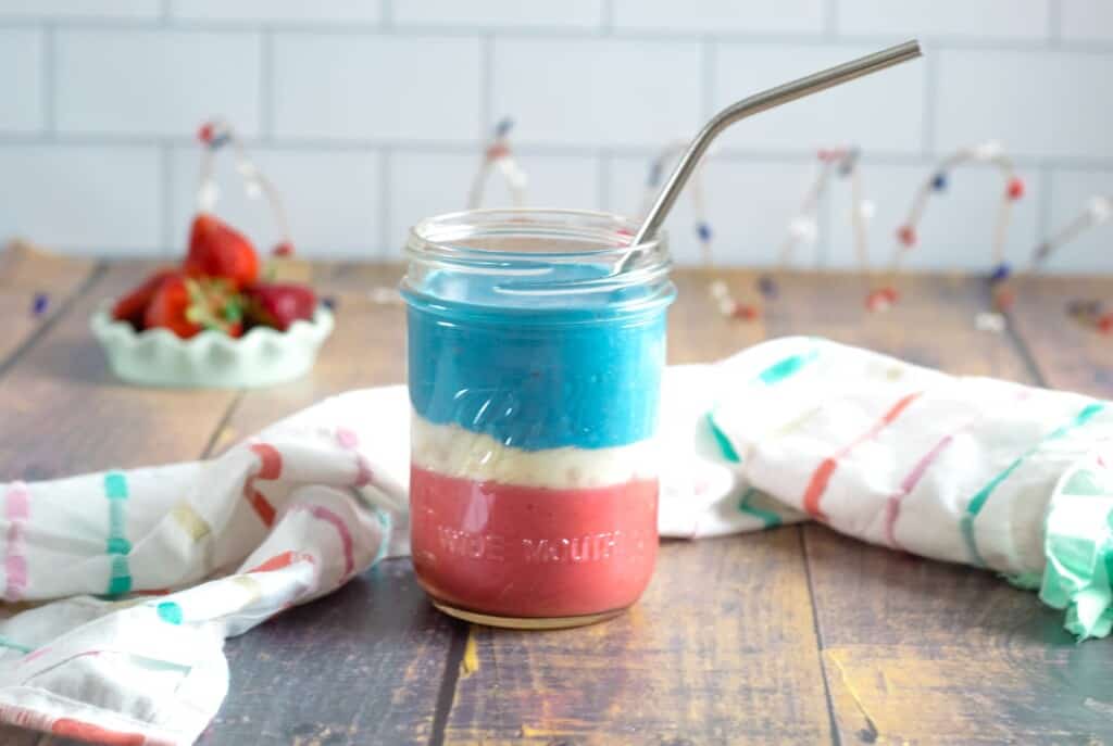 Mason jar with red white and blue. smoothie layered with a straw coming out of it on a table.