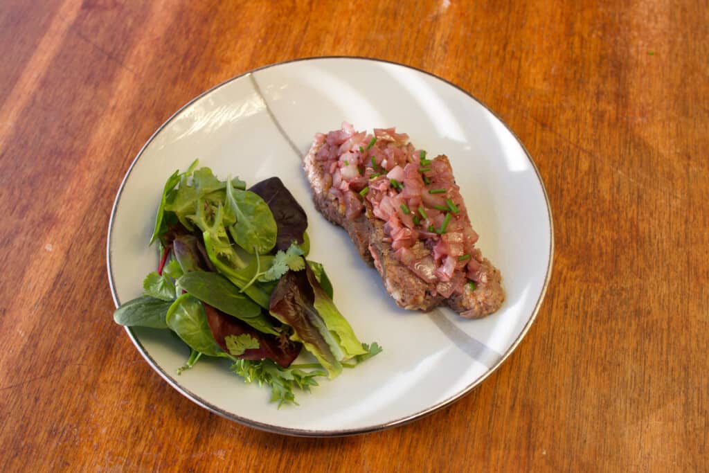 A plate of chaliapan steak and some greens on the side. 