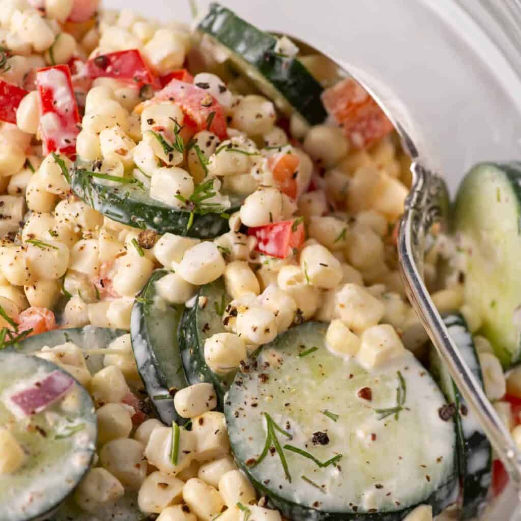 Corn and cucumber salad in a bowl with a serving spoon tucked inside.