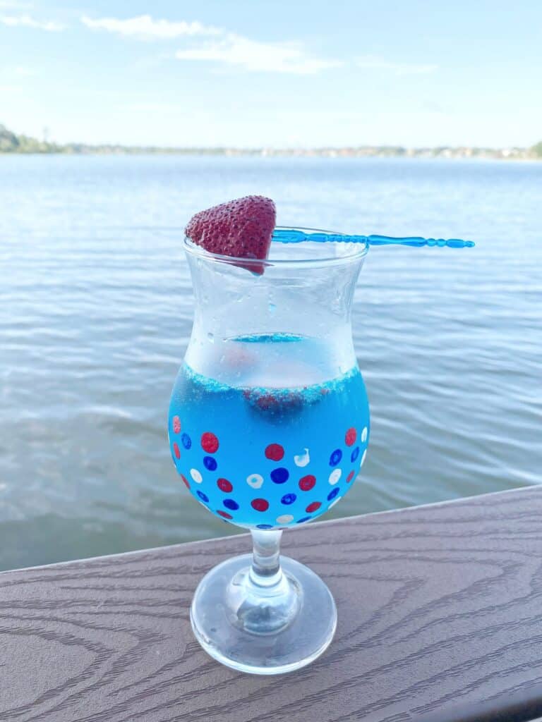 Glass of patriotic mimosa with a strawberry garnish sitting on a ledge in front of the lake.