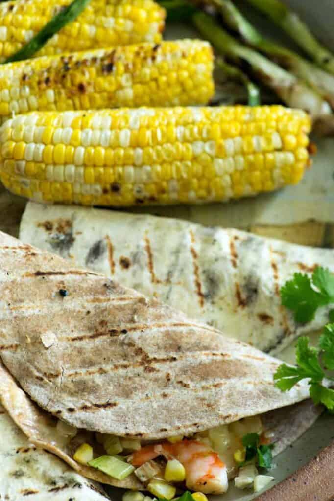 What To Serve With Corn On The Cob. Corn tortillas with veggies and shrimp grilled on a platter with corn on the cob sitting alongside it. 