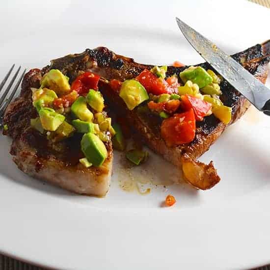What To Serve With Corn On The Cob. Grilled ribeye with hatch chile avocado salsa on top with a fork and knife on the plate alongside it. 
