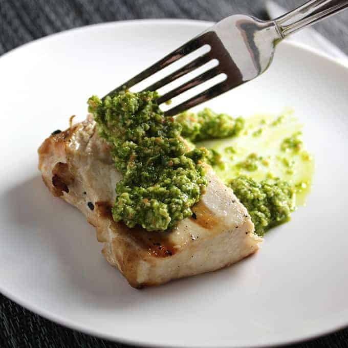 A fork cutting into grilled swordfish that has kale pesto topping it. 